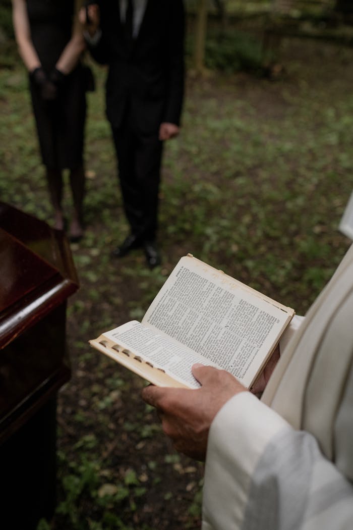 Pastor reading from the Holy Bible during an outdoor funeral service with mourners present.