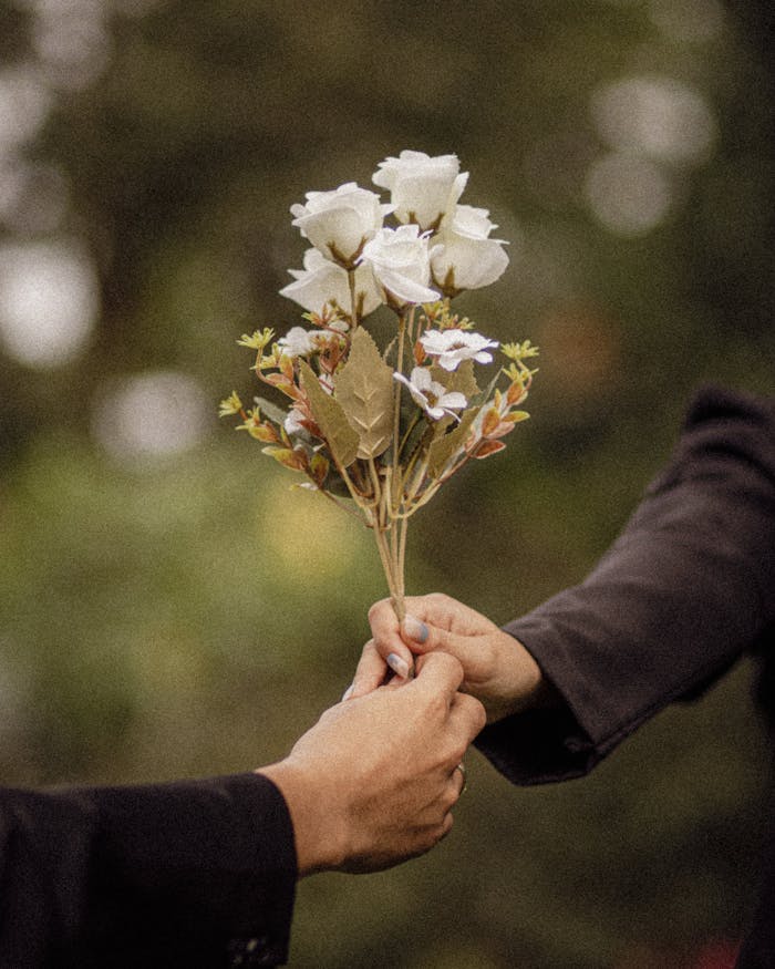 Two people exchange a bouquet of white flowers outdoors, symbolizing romantic connection.