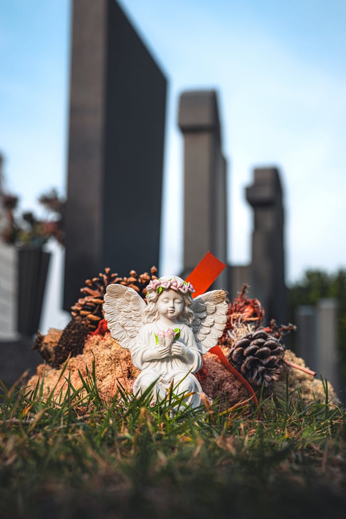 A serene angel statue adorned with flowers against a backdrop of grave markers in a cemetery.