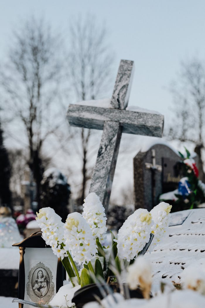 services-03 A solemn cemetery scene featuring a stone cross and fresh flowers in a winter setting.