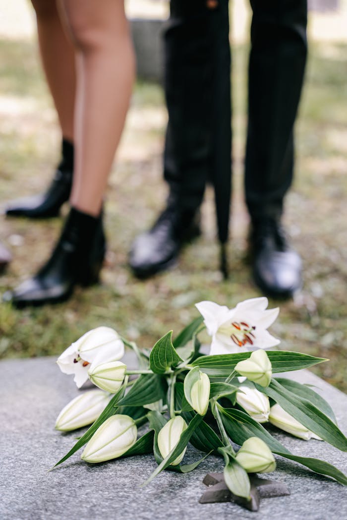 White lily flowers on a tombstone, symbolizing grief and loss at a cemetery.